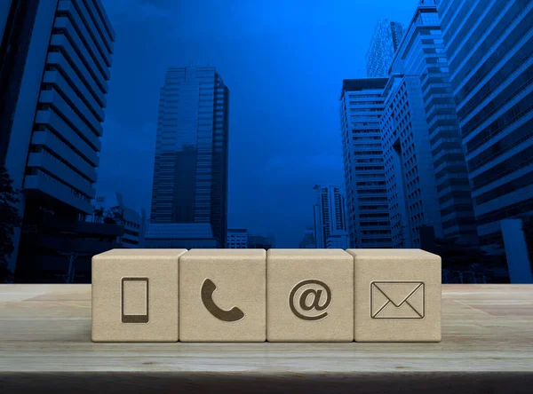 Mobile phone, telephone, email address, mail icon on wood block cubes on wooden table over modern office city tower and skyscraper, Business customer service and support online concept