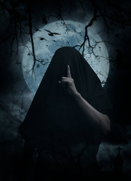 Grim reaper showing silence sign with finger standing over cross, church, crow, birds, dead tree, full moon and cloudy spooky sky, Halloween mystery concept