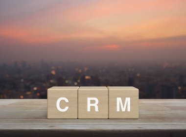 CRM letter on wood block cubes on wooden table over blur of cityscape on warm light sundown, Customer Relationship Management concept