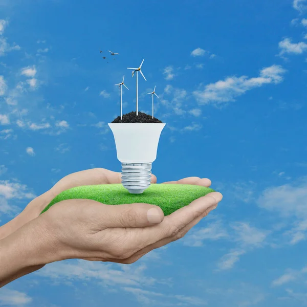 Wind turbines on soil with light bulb in hands over blue sky and birds, Green ecology and saving energy concept