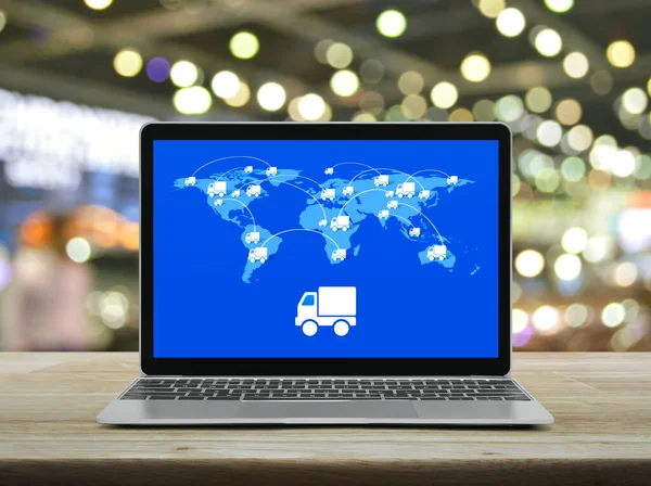 Delivery truck flat icon with connection line and world map on modern laptop computer screen on wooden table over blur light and shadow of shopping mall, Business transportation online concept, Elements of this image furnished by NASA