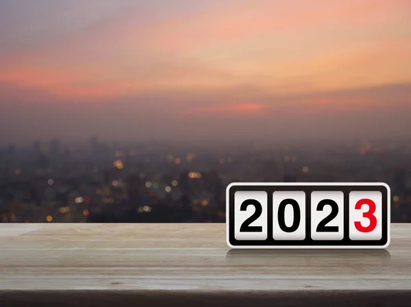 Retro flip clock with 2023 text on wooden table over blur of cityscape on warm light sundown, Happy new year 2023 cover concept