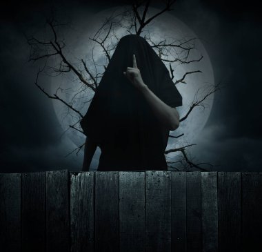 Grim reaper showing silence sign with finger standing over dead tree, full moon and cloudy spooky sky, Halloween mystery concept
