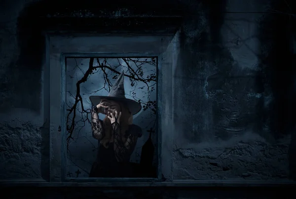 Scary halloween witch standing in old damaged window with wall over cross, church, birds, dead tree and cloudy spooky sky, Halloween mystery concept