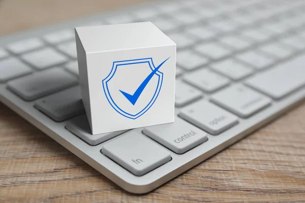 Security shield with check mark flat icon on white block cube with modern computer keyboard on wooden table, Technology internet cyber security and anti virus online concept