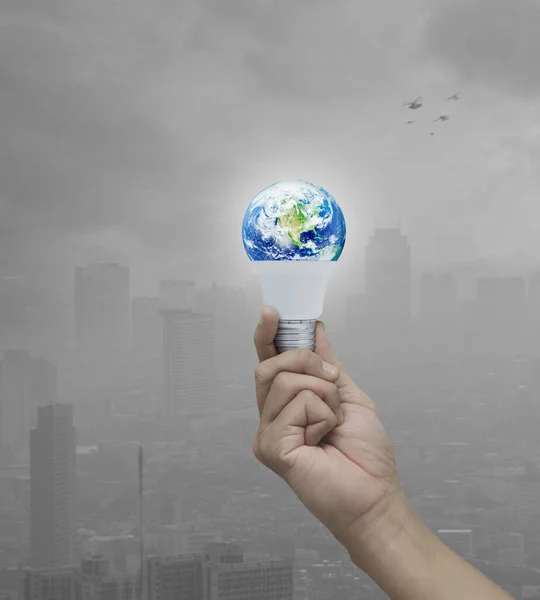 Hand holding earth globe inside led light bulb with fresh green tree leaves over pollution city tower with birds, Green ecology and saving energy concept, Elements of this image furnished by NASA