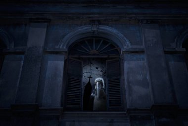 Küçük emir subayı leylek kuşu eski hasarlı pencerenin önünde duruyor, duvarları haçın üzerinde, kilise ve ürkütücü bulutlu gökyüzü, Cadılar Bayramı gizemi