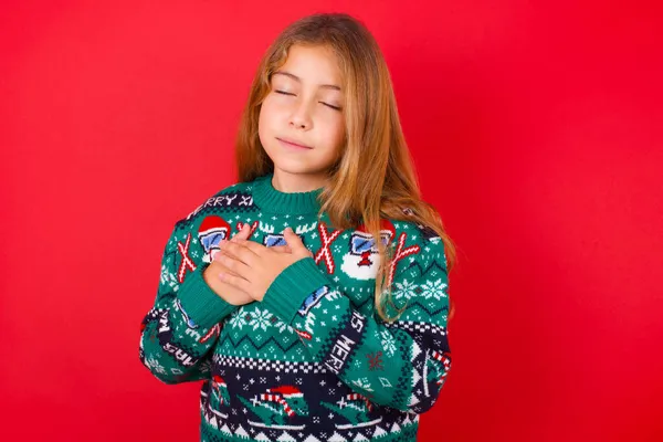 Красивая Девушка Рождественском Свитере Закрывает Глаза Держит Руки Груди Рядом — стоковое фото