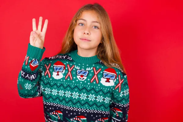 クリスマスセーターを着た美しい女の子は自信と幸せを笑いながら指ナンバー3を指で指で指さす — ストック写真