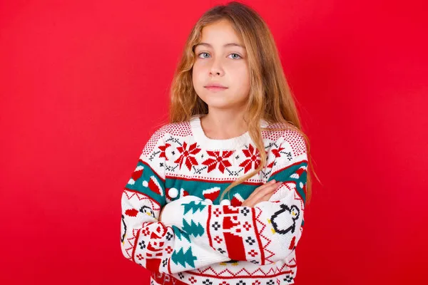 クリスマスのセーターを身に着けている自己自信の深刻な落ち着いた美しい女の子は折られた腕と立っています プロの雰囲気は主張的なポーズで立っています — ストック写真