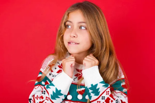 クリスマスのセーターを身に着けている美しい女の子は拳をひねり 何か素敵なことが起こったのを待って 唇を噛み 結果の発表を待ちます — ストック写真