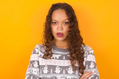 Utanmış bir kadının Noel süveteri giymesi sarı stüdyo arka planının ağzını açık tutmasını sağlıyor. İnanılmaz bir yenilik duyuyor sersemlemiş gibi bakıyor.