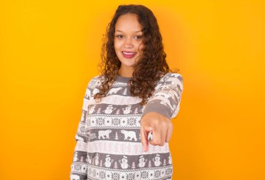 Heyecanlı, pozitif bir kadın, Noel süveteri giyen, sarı stüdyo arka planda çalışan, işaret parmağı olan, çok komik bir şey görüyor. Vay canına, inanılmaz.