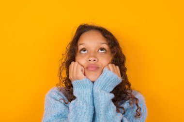 Sarı arka planda mavi süveter giyen üzgün kıvırcık kadın portresi.