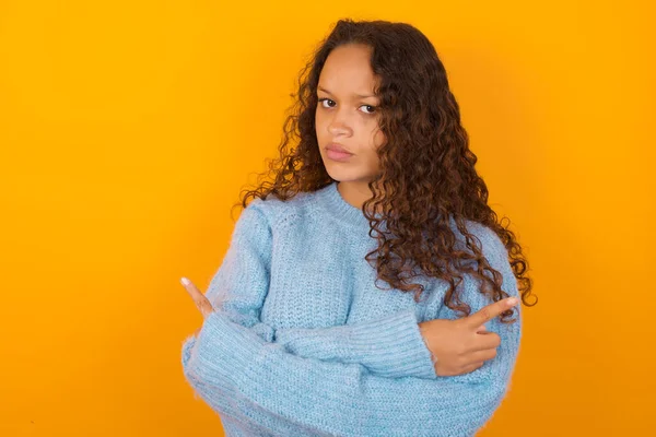 Serious Curly Woman Wearing Blue Sweater Yellow Studio Background Crosses — Stock Photo, Image