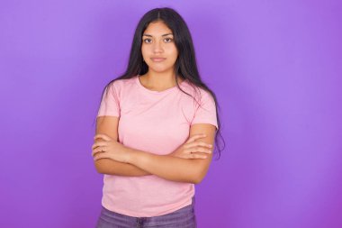 Mor arka planda pembe tişört giyen ciddi düşünceli esmer kız havalı, kendine güvenen girişimci çapraz eli gibi hissediyor..