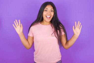 İyimser esmer, pembe tişörtlü kız mor arka planda, sevinçten avuçlarını kaldırıyor, birinden müthiş bir hediye almaktan mutlu, yüksek sesle bağırıyor. Heyecanlı model çığlıkları.