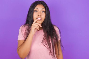 Gergin, şaşkın esmer, pembe tişörtlü kız mor arka planda, ağzı açık, ani haberlere tepki veriyor.. 