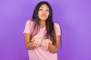 Mor arka planda pembe tişört giyen esmer İspanyol kız dudaklarıyla öpücük yolluyor ve hava öpücüğü vermek için avuç içi tutuyor..