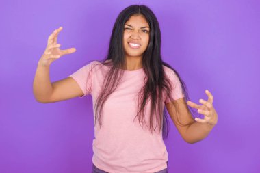 Mor arka planda pembe tişört giyen esmer İspanyol kız öfkeden kudurmuş, elleri boğazlamaya çalışıyor..