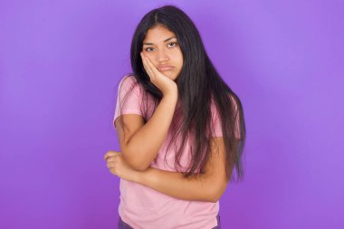 Çok sıkılmış esmer, pembe tişörtlü bir kız mor arka planda el ele tutuşurken onu başka bir çapraz elle desteklerken yorgun ve hasta görünüyor. 