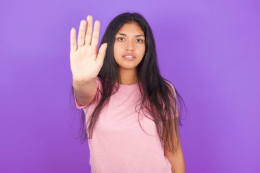 Mor arka planda pembe tişört giyen esmer İspanyol kız avuç içiyle şarkı söylemeyi kesiyor. Yüzünde olumsuz ve ciddi bir jest olan uyarı ifadesi.
