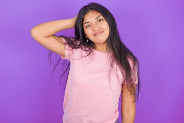 Mor arka planda pembe tişört giyen esmer İspanyol kızın kafası karışmış ve bir şeyi merak ediyor. El ele tutuşmak, şüpheyle emin olmak. Düşünceli kavram.