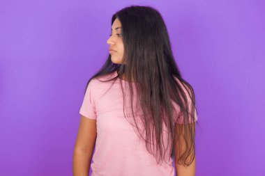 Yan profil fotoğrafını çek İspanyol esmer kız pembe tişört giyiyor mor arka plan üzerinde gülümsemiyor, dikkatli dinle konsantre ol.