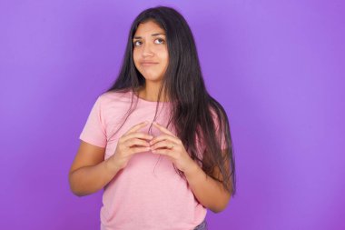 Mor arka planda pembe t-shirt giyen esmer kız parmaklarını kuleye geçirir ve gizemli görünür.