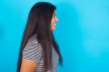 Mavi arka planda çizgili tişört giyen gülümseyen İspanyol genç kızın profil portresi