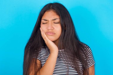 Dişi ağrılı, mavi arka planda çizgili tişört giyen İspanyol genç kız. 