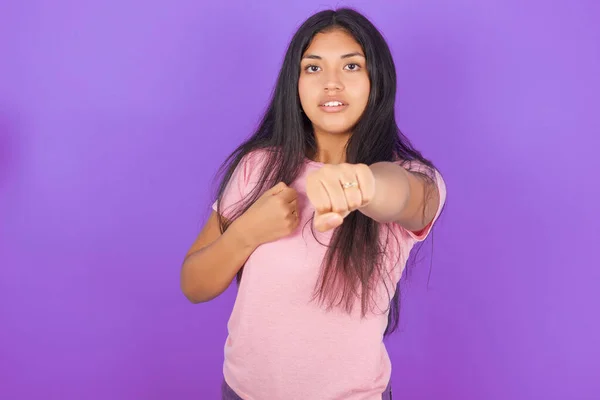 西班牙裔黑发女孩穿着粉色T恤 背景是紫色的 她用拳头打斗 挑衅和愤怒的攻击 威胁和暴力 — 图库照片