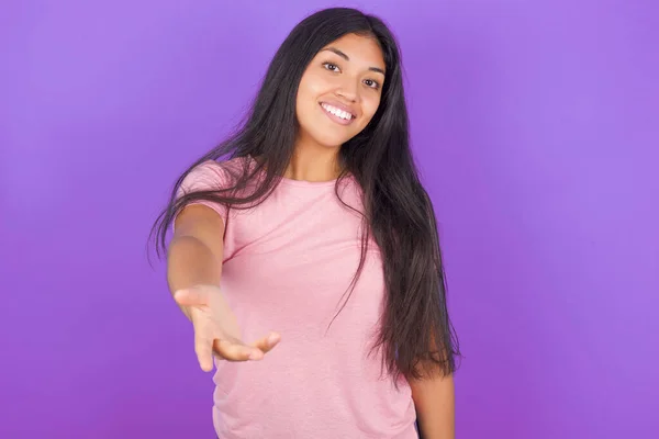 ピンクのTシャツを着たヒスパニック系のブルネットの女の子は 挨拶や歓迎として握手を提供する優しい笑顔紫色の背景に 成功事業 — ストック写真