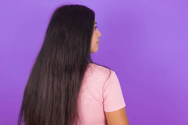 紫色の背景にピンクのTシャツを着ているヒスパニックなブルネットの女性の背面の景色 スタジオショット — ストック写真