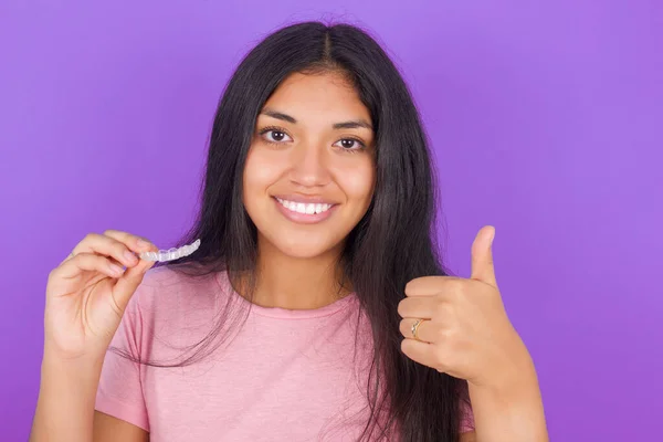 紫の背景にピンクのTシャツを着たヒスパニック系のブルネットの女の子は この新しい治療をお勧めします 歯科医療の概念 — ストック写真