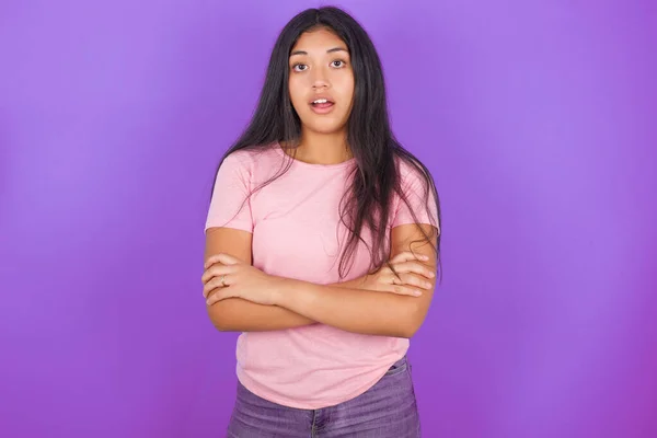 紫色の背景にピンクのTシャツを着たショックを受けたヒスパニック系のブルネットの女の子は広く口を開けておきます 信じられないほどの目新しさを聞く — ストック写真