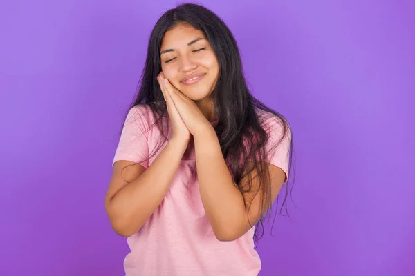 ピンクのTシャツを着た若いヒスパニック少女は 押された手のひらに紫色の背景のリーンを着て目を閉じ 何かについて楽しい笑顔の夢を持っています — ストック写真