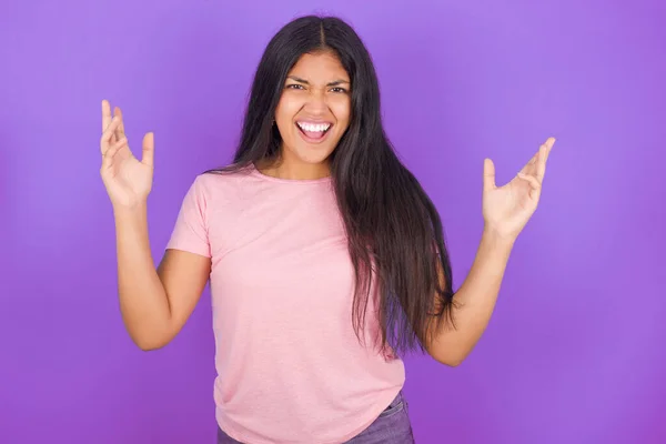 紫の背景の上にピンクのTシャツを着たクレイジー激怒した若いヒスパニック系の女の子が大声で叫び ジェスチャーを怒って激怒します 否定的な人間の感情の概念 — ストック写真