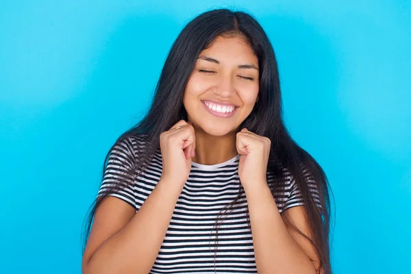 青の背景に縞模様のTシャツを着た若いヒスパニック系の女の子が喜んで 何か楽しい コピースペースを想像します 心地よい感情の概念 — ストック写真
