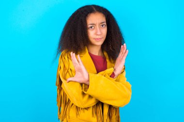 Afro saçlı, mavi arka planda sarı ceketli Afro-Amerikalı bir genç kız yüzünde kızgın bir ifadeyi reddediyor ve olumsuz işaretler veriyor..