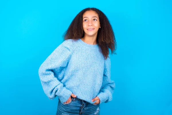 青い背景に青いセーターを着たアフロスタイルの成功したアフリカ系アメリカ人のティーンエイジャーの少女の肖像画は 広く自信を持って表現で笑顔 自信とビジネスコンセプト — ストック写真