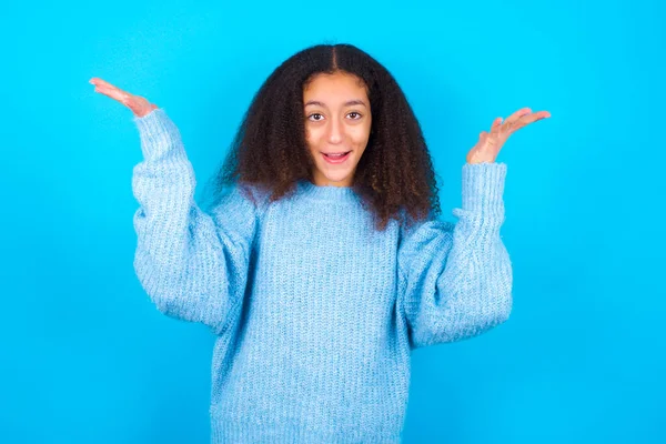 青い背景に青いセーターを着たアフロスタイルのアフリカ系アメリカ人の10代の少女が手を上げて 彼の大きな成果を喜びに満ちた目を持っています 成功の概念 — ストック写真