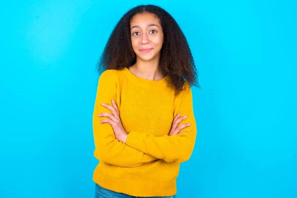 青い背景の上に黄色のセーターを着てアフロの髪のスタイルを持つ自信を持って深刻な穏やかなアフリカ系アメリカ人のティーンエイジャーの女の子は 腕が折り畳まれて立っている プロの雰囲気スタンドで積極的なポーズ — ストック写真
