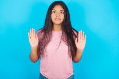 Ciddi bir genç kız avuç içlerini kameraya çeker, jestleri durdurur, duygularını kontrol etmesini ve gergin olmamasını ister. Pembe tişört giyen esmer, güzel bir kadın mavi arka plana poz veriyor.