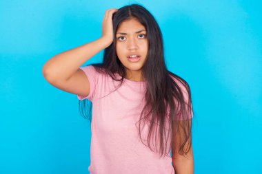 Şok olmuş yüzü olan utangaç bir kız, şaşkınlığını dile getiriyor, Bilmece modelleri içeride poz veriyor. Pembe tişört giyen esmer, güzel bir kadın mavi arka plana poz veriyor.
