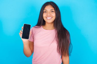 Gülümseyen kız. Kopyalama alanı oluşturun. Genç, güzel, boş ekranlı cep telefonu tutan Latin kız.