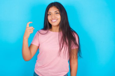  Çince işaret dilinde dokuz numarayı işaret eden kız Jiu. Pembe tişört giyen esmer, güzel bir kadın mavi arka plana poz veriyor.