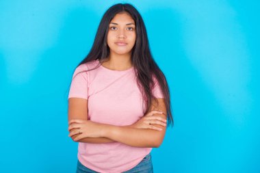 Kendine güveni tam, sakin, güzel Latin kız kollarını kavuşturmuş duruyor. Profesyonel titreşimlerin kendine güvenen pozlarda durduğunu gösterir.