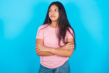 Düşünceli, düşünceli, genç, güzel, Latin bir kız kollarını kavuşturmuş, düşünceli bir ifadeyle ne yapacağını düşünüyor.