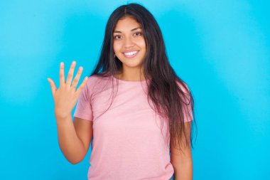  Gülümseyen ve arkadaş canlısı görünen bir kadın. Beş ya da beş numarayı gösteriyor. Eli önde, geri sayıyor. Pembe tişört giyen esmer, güzel bir kadın mavi arka plana poz veriyor.